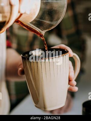 primo piano del caffè versato da versare in una tazza di caffè abbronzata Foto Stock
