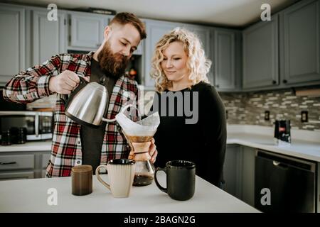 l'uomo versa l'acqua calda nel caffè e si versa mentre la moglie guarda sopra Foto Stock