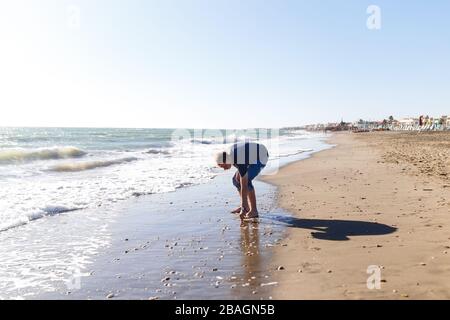 biondo ragazzo turistico in jeans godendo la spiaggia e il mare Foto Stock