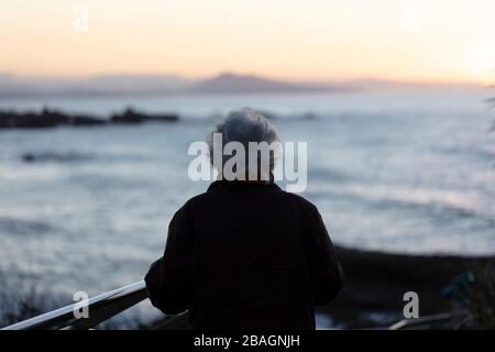 Donna anziana che guarda verso l'oceano. Foto Stock