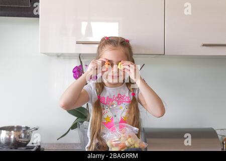 Bambina seduto in cucina e mettendo gnocchi sui suoi occhi. Concetto di quarantena del coronavirus. Ti sentirai come a casa. Foto Stock