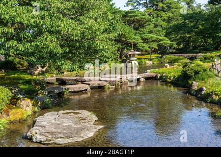 Laghetto panoramico attraversato da un piccolo ponte di pietra nel giardino Kenroku-en, Kanazawa, Giappone Foto Stock