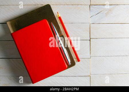 Il notebook rosso si trova su un notebook dorato, sul tavolo in legno bianco accanto a una matita rossa Foto Stock