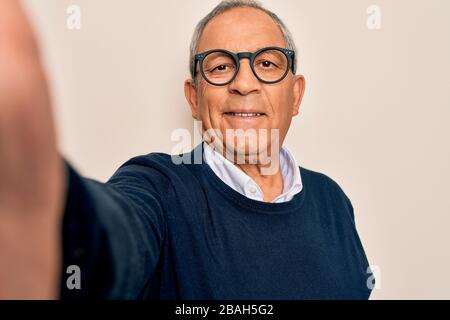 Uomo anziano con i capelli grigi e gli occhiali che fanno il selfie con la macchina fotografica con un volto felice in piedi e sorridente con uno spettacolo di sorriso sicuro Foto Stock
