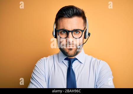 Giovane operatore aziendale che indossa cuffie per il servizio clienti del call center, espressione scettica e nervosa, disapprovante sul viso con braccia incrociate. Foto Stock
