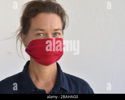 La donna caucasica pone per la macchina fotografica con la sua maschera fai da te (fatta da una vecchia maglietta manica) durante la pandemia del virus corona 2019/20. Foto Stock
