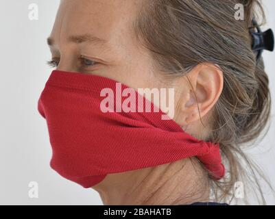 La donna caucasica si pone per la telecamera con la sua maschera facciale fai da te (realizzata da una vecchia maglietta) durante la pandemia del virus corona 2019-20 . Foto Stock