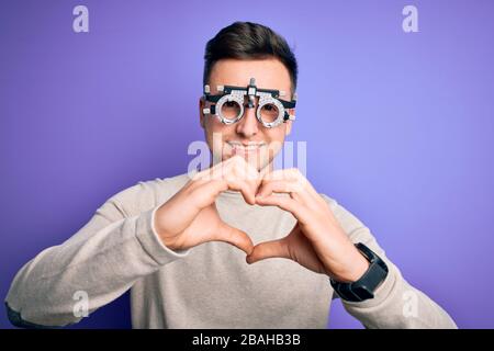 Giovane bell'uomo caucasico che indossa occhiali optometrici su sfondo viola sorridente nell'amore mostrando il simbolo del cuore e la forma con le mani. Romantico c Foto Stock