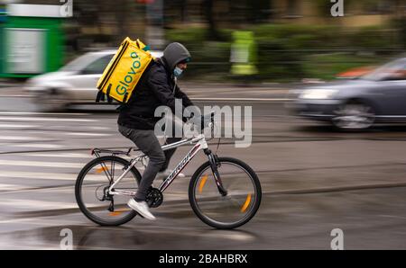 Bucarest, Romania - 23 marzo 2020: Una maschera di consegna del corriere di alimento di Glovo su una bici. I ristoranti sono chiusi e solo le consegne sono consentite durante Foto Stock