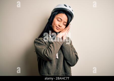 Giovane bella donna cinese che indossa casco su sfondo bianco isolato dormire stanco sognare e posare con le mani insieme mentre sorride Foto Stock