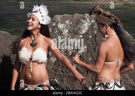 Rapa Nui ballerini in costume tradizionale, con la donna che applica body paint al braccio della sua amica sull'Isola di Pasqua Foto Stock
