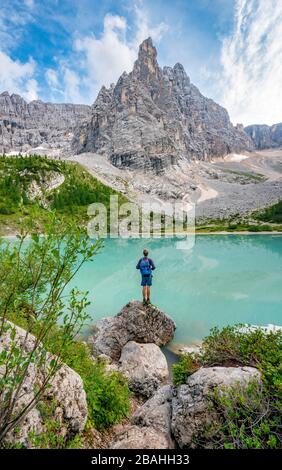 Giovane uomo in pietra, escursionista presso il lago verde turchese di Sorapis, Lago di Sorapis, vetta di montagna Dito di Dio, Dolomiti, Belluno, Italia Foto Stock