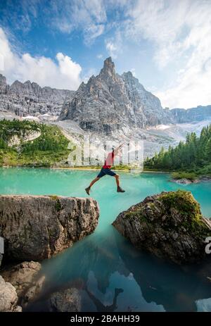 L'escursionista salta da pietra a pietra al lago verde-turchese Sorapis, Lago di Sorapis, nella montagna posteriore Dito di Dio, Dolomiti, Belluno, Italia Foto Stock