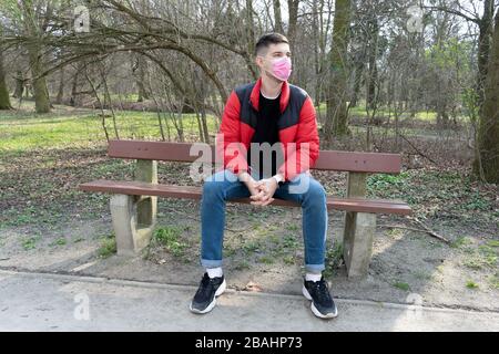 Ritratto di bruna in un bendaggio chirurgico seduto nel parco sul banco, coronavirus, malattia, infezione, quarantena, maschera medica Foto Stock