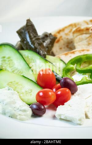 Vista poco profonda del semplice piatto di meze greco; con verdure, pita, feta e foglie di uva Foto Stock