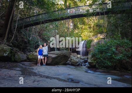 Una coppia turistica che si erge insieme sotto un passaggio sopraelevato in una delle cascate del Parco forestale di Buderim sulla Sunshine Coast nel Queensland. Foto Stock