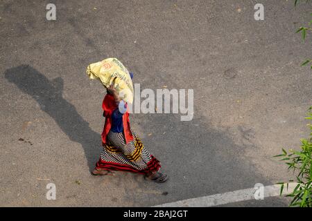 New Delhi, India - 21 marzo 2020: Donna indiana indossando una passeggiata sari mentre trasporta e bilancia un sacco pesante di cemento sulla sua testa, lavorando ad un contro Foto Stock