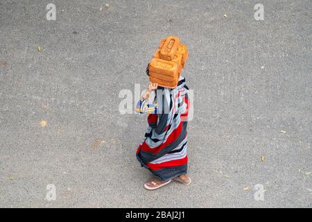 New Delhi, India - 21 marzo 2020: Donna indiana indossando una passeggiata sari mentre trasporta e bilanciano mattoni sulla sua testa, lavorando in un cantiere Foto Stock