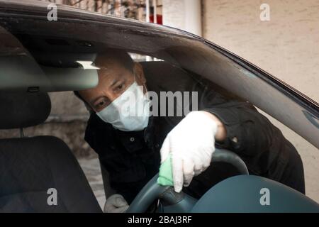 L'uomo turco di mezza età disinfetta il volante della sua auto come precauzione per il virus pandemico della corona Foto Stock