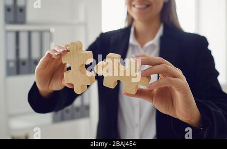 Mani senza volto di una donna d'affari con puzzle in legno in mani in ufficio. Foto Stock