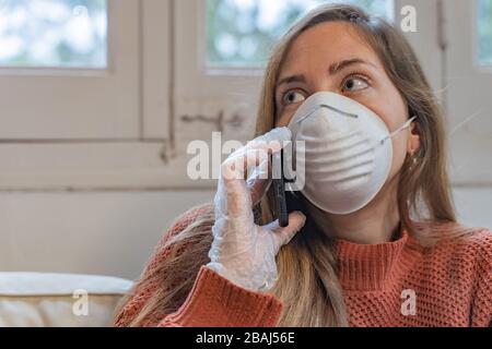 Coronavirus. Donna con maschera facciale e guanti in gomma che puliscono il suo spazio di lavoro con un disinfettante a casa durante l'epidemia di coronavirus. Prevenzione Foto Stock
