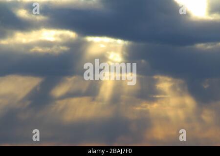 Il sole al tramonto o all'alba dietro le nuvole, splende attraverso. I raggi del sole nel cielo. Foto Stock