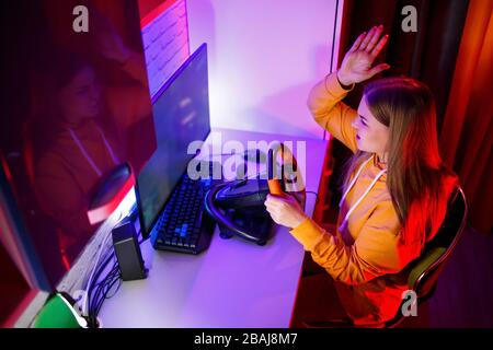 ragazza gamer che gioca a correre su un computer. Utilizza un volante. Gioco emotivo Foto Stock