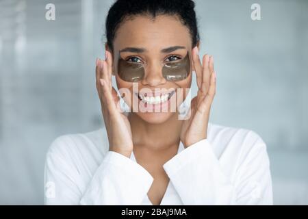 Felice bella donna africana applicare sotto gli occhi idrogel patch Foto Stock