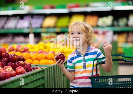 Bambino al supermercato che acquista frutta e succo. Negozio di alimentari per bambini. Ragazzino con carrello che sceglie verdure fresche in negozio locale. Foto Stock