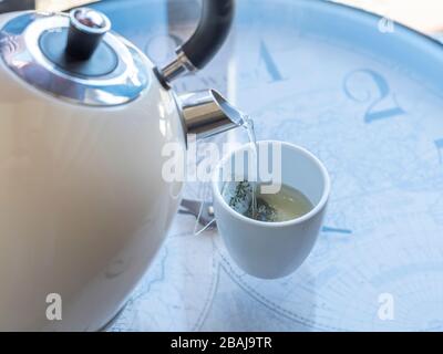 bollitore elettrico con acqua bollente per il tè alle erbe. Selettiva focalizzata su una tazza da tè con una borsa da tè Foto Stock