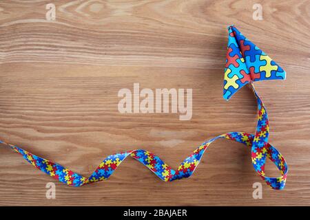 Consapevolezza autismo giorno o mese. Piano di carta in stile origami con nastro puzzle di consapevolezza autismo su sfondo di legno. Foto Stock
