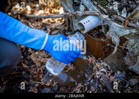 Ecologo prelievo di campioni di acqua da una fonte naturale in guanti protettivi Foto Stock