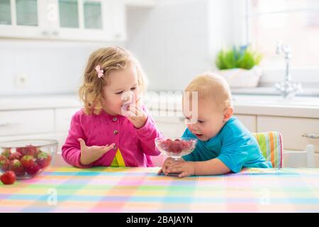 Bambini che consumata la colazione. Bambini bevendo latte e mangiando cereali con frutta. Ragazzino e bambina al tavolo da pranzo bianco in cucina alla finestra. I bambini mangiano su Foto Stock