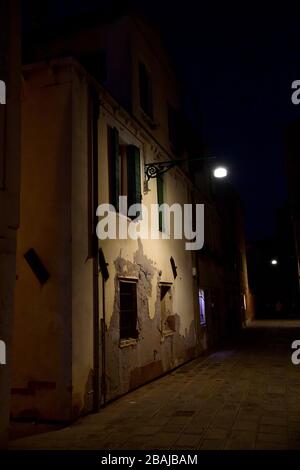 Lampada retro sulla casa veneziana che dà ampia luce in vicolo scuro sullo sfondo di una casa tradizionale fondamentalmente coperto al buio con solo luce Foto Stock