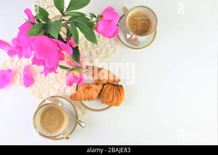 La prima colazione con due tazze di caffè e croissant, bouquet di fiori di colore rosa peonie Foto Stock