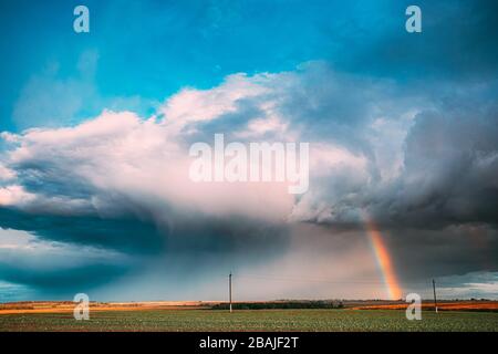 Cielo drammatico durante la pioggia con Arcobaleno su orizzonte al di sopra del paesaggio rurale campo. Agricola e previsioni meteo concetto. Campagna prato in autunno Foto Stock