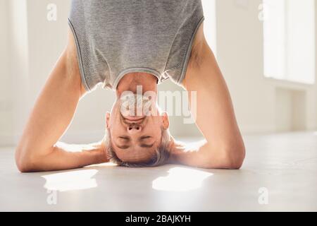 L'uomo che pratica lo yoga e che sta in piedi nella posa del headstand Foto Stock