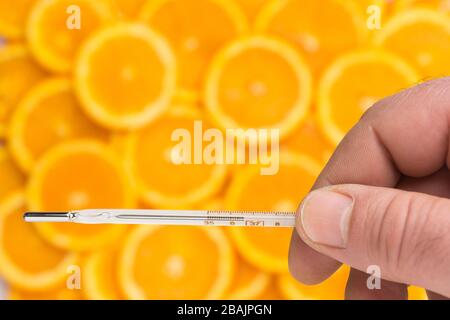 La mano corta tiene un termometro di mercurio sopra un modello delle fette fresche di arancio come concetto di supplemento di nutrizione contro l'influenza Foto Stock