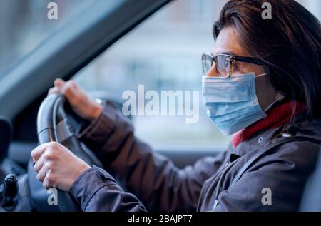 Una donna che indossa una maschera protettiva durante la guida Foto Stock