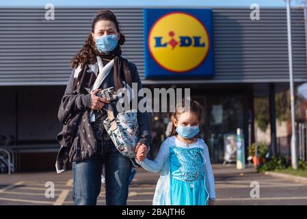 Ritratto di mamma e figlia in piedi con maschere facciali fuori di un supermercato, Coronavirus UK Foto Stock