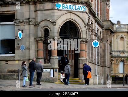 La gente osserva le distanze sociali mentre accodano fuori di un ramo della banca di Barclays nel centro della città di Wolverhampton mentre il Regno Unito continua in blocco per contribuire a frenare la diffusione del coronavirus. Foto Stock