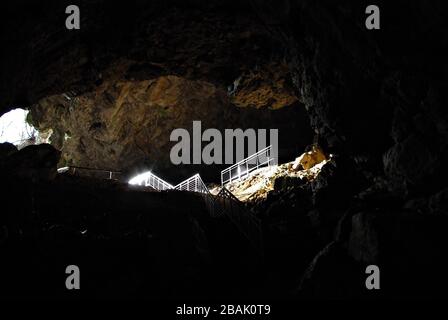 All'interno di una grotta umida scura con le scale di uscita illuminate in vista. Foto Stock