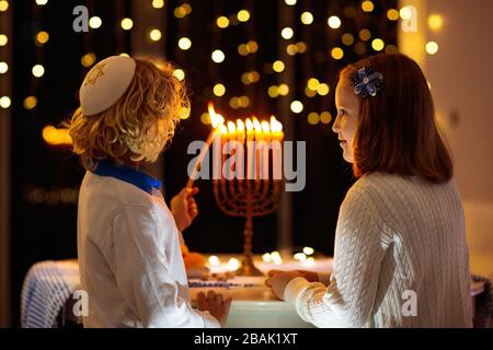 I bambini celebrano Hanukkah. Festa ebraica delle luci. Bambini che illuminano candele sulla tradizionale menorah. Ragazzo in kippah con dreidil e Sufganiyah doug Foto Stock