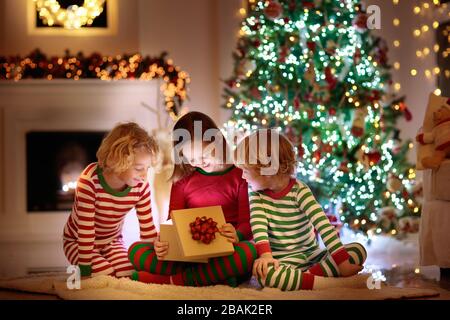 I bambini ad albero di Natale e camino vigilia di Natale. Famiglia con bambini festeggiano il Natale a casa. Un ragazzo e una ragazza in pigiama corrispondente decorazione di Natale Foto Stock