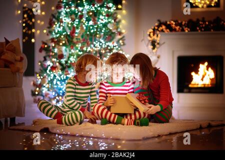 I bambini ad albero di Natale e camino vigilia di Natale. Famiglia con bambini festeggiano il Natale a casa. Un ragazzo e una ragazza in pigiama corrispondente decorazione di Natale Foto Stock