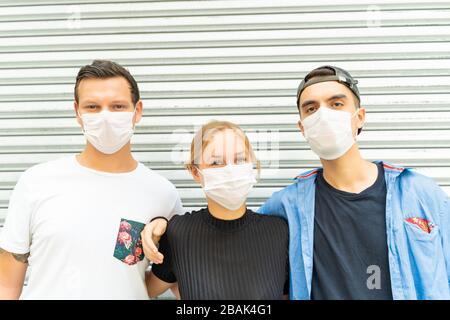 Ritratto di tre persone di diverse etnie indossando una maschera facciale che si protegge dal coronavirus nella strada Foto Stock