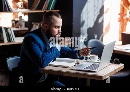 Un uomo d'affari con bearded serio conduce le conversazioni telefoniche su un telefono mobile al calcolatore. L'uomo infelice si lamenta al telefono. Emitations di rabbia in Foto Stock