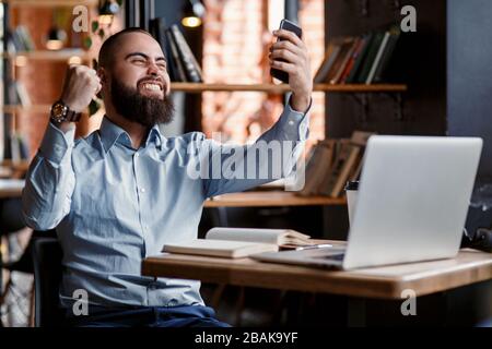 Euforico felice uomo d'affari urlare leggere le buone notizie in linea che celebrano il successo di affari, grande risultato che guarda il gioco sul laptop, eccitato dalla vittoria, bettin Foto Stock