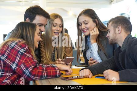 Gruppo di amici che si appendono a vicenda seduti in un bar utilizzando i loro telefoni cellulari - giovani , millennial holding cellulari , godendo onli Foto Stock