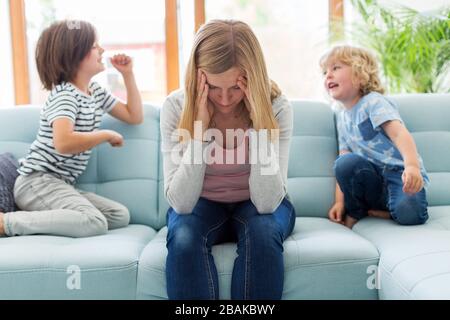 Madre con mal di testa e bambini che saltano sul divano Foto Stock